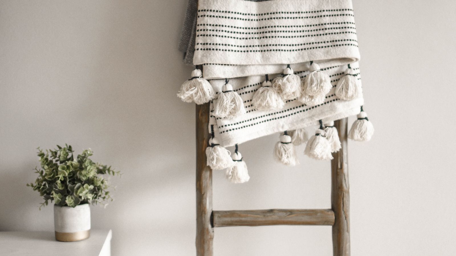 Wooden blanket ladder leaning against a bedroom wall holding folded throws
