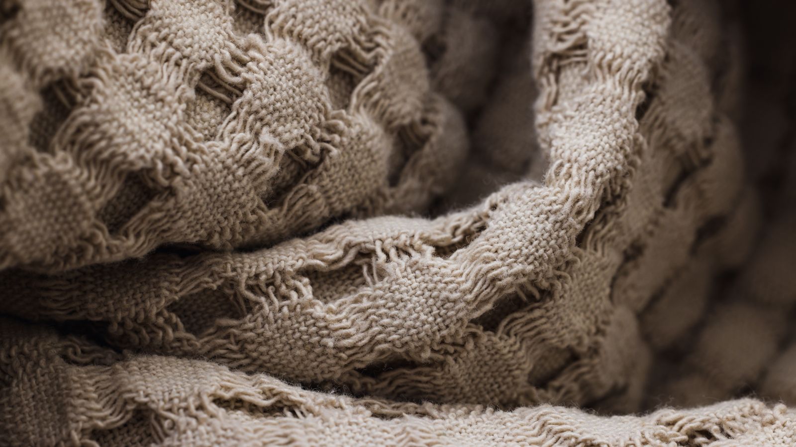 Folded waffle weave blanket and lightweight throws stacked on a bed for a seasonal linen rotation