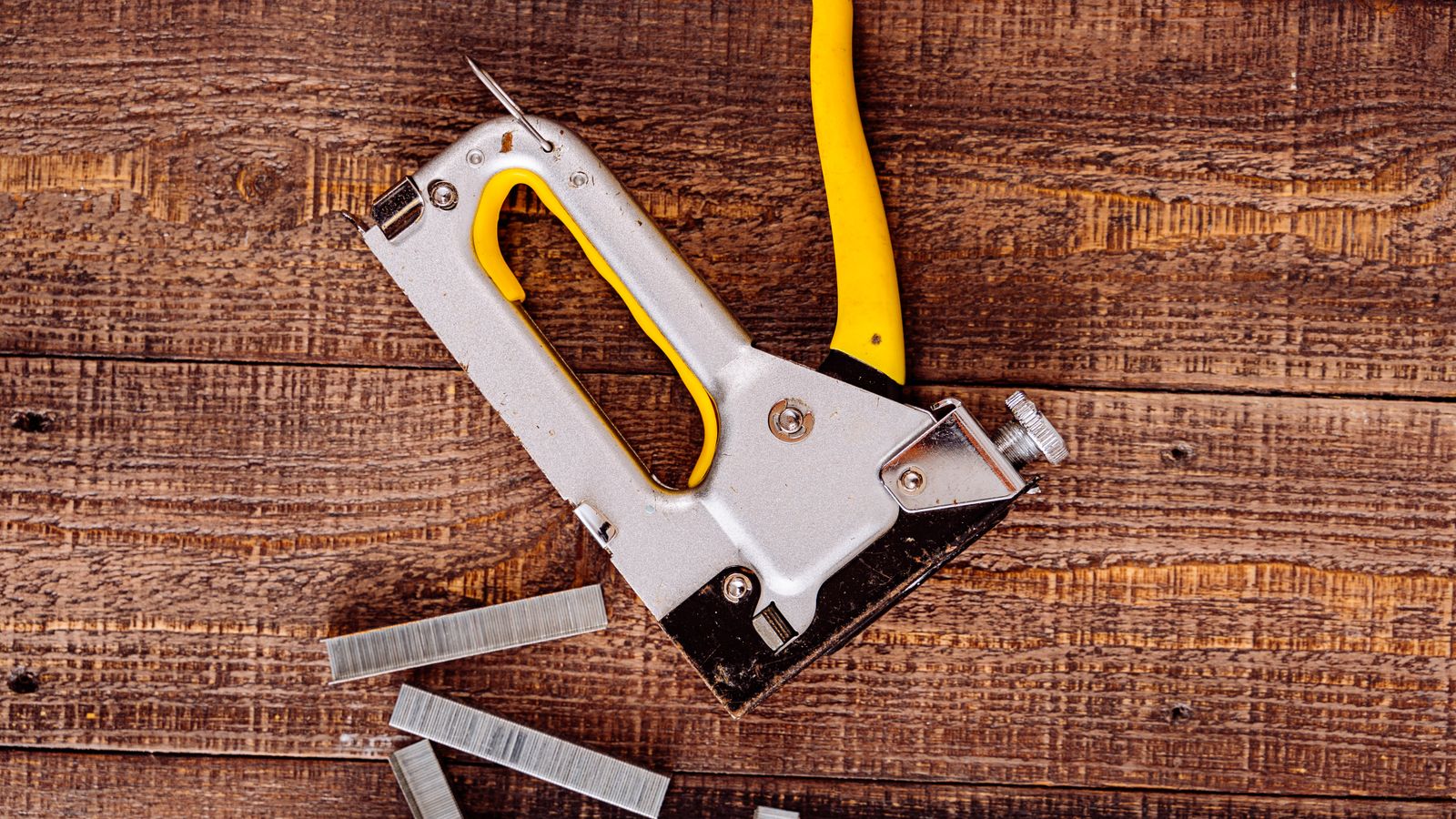Person using an upholstery staple gun to secure fabric to a wooden chair frame