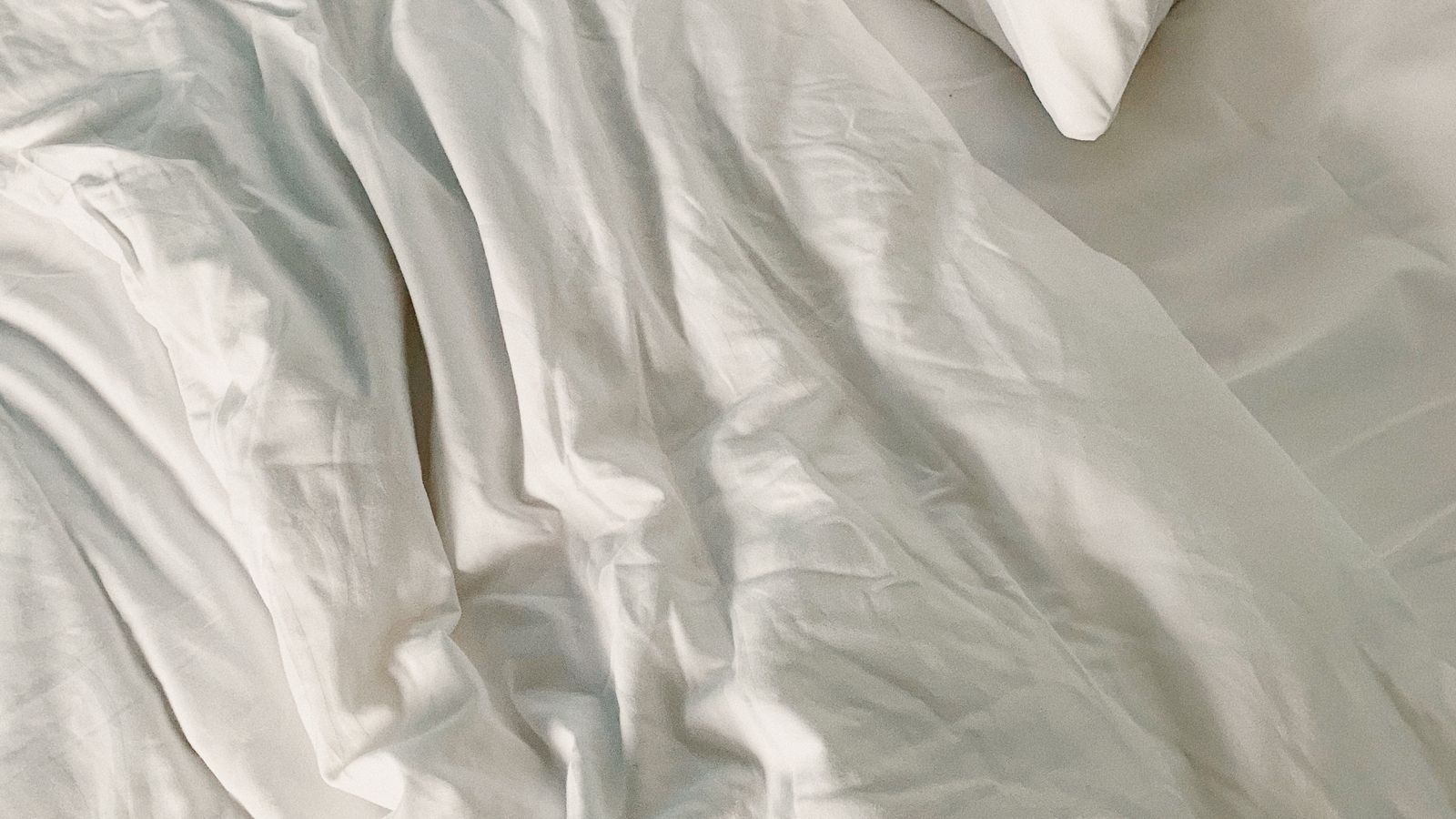 Folded cooling comforter resting on a bed with light, breathable fabric