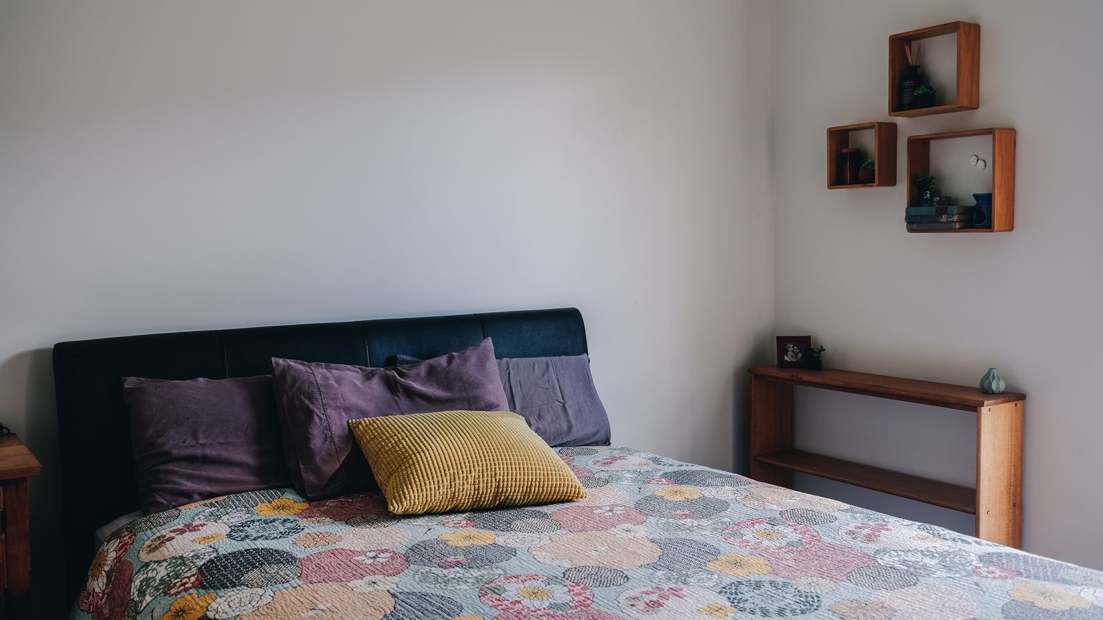Wall-mounted headboard storage shelf with books and a lamp above a bed