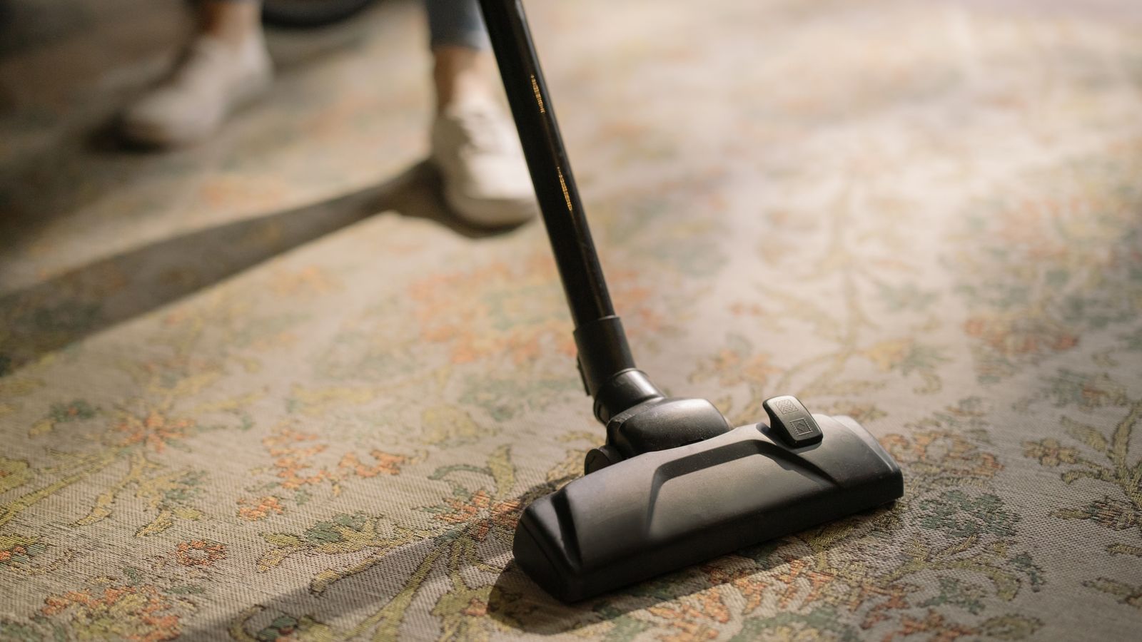 Person vacuuming a thick carpet with an upright vacuum cleaner in a living room