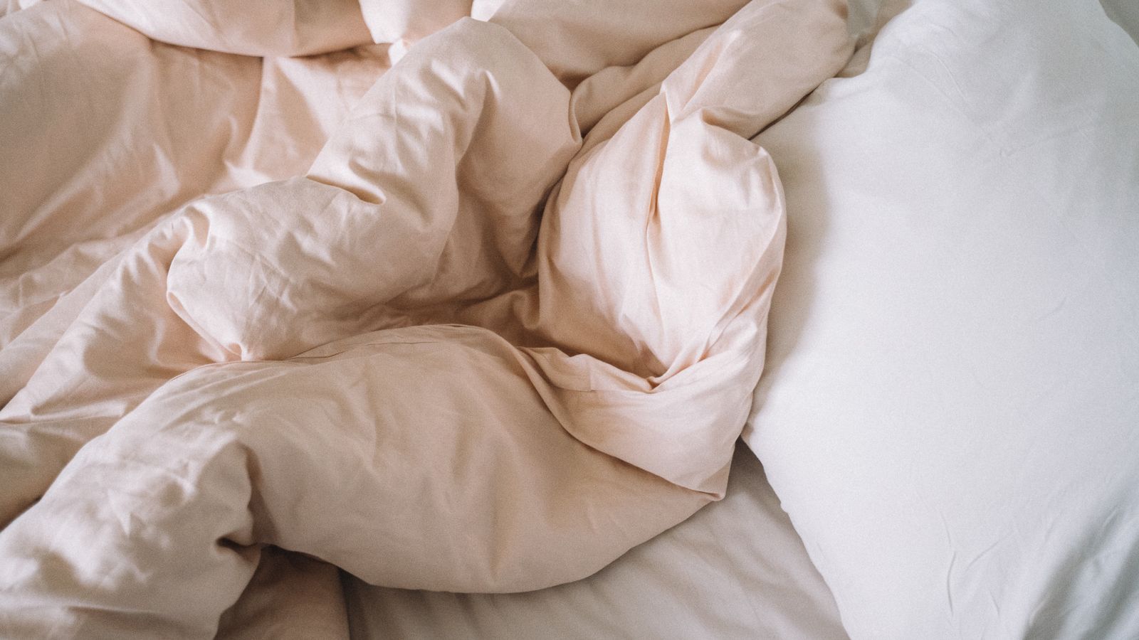Hands smoothing a fitted jersey knit sheet over a mattress corner in a small bedroom