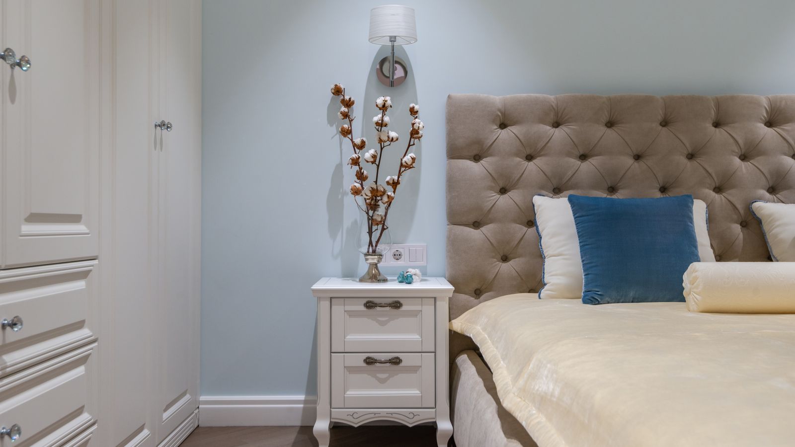 Small bedroom with organized nightstand, lamp, and tidy storage surfaces
