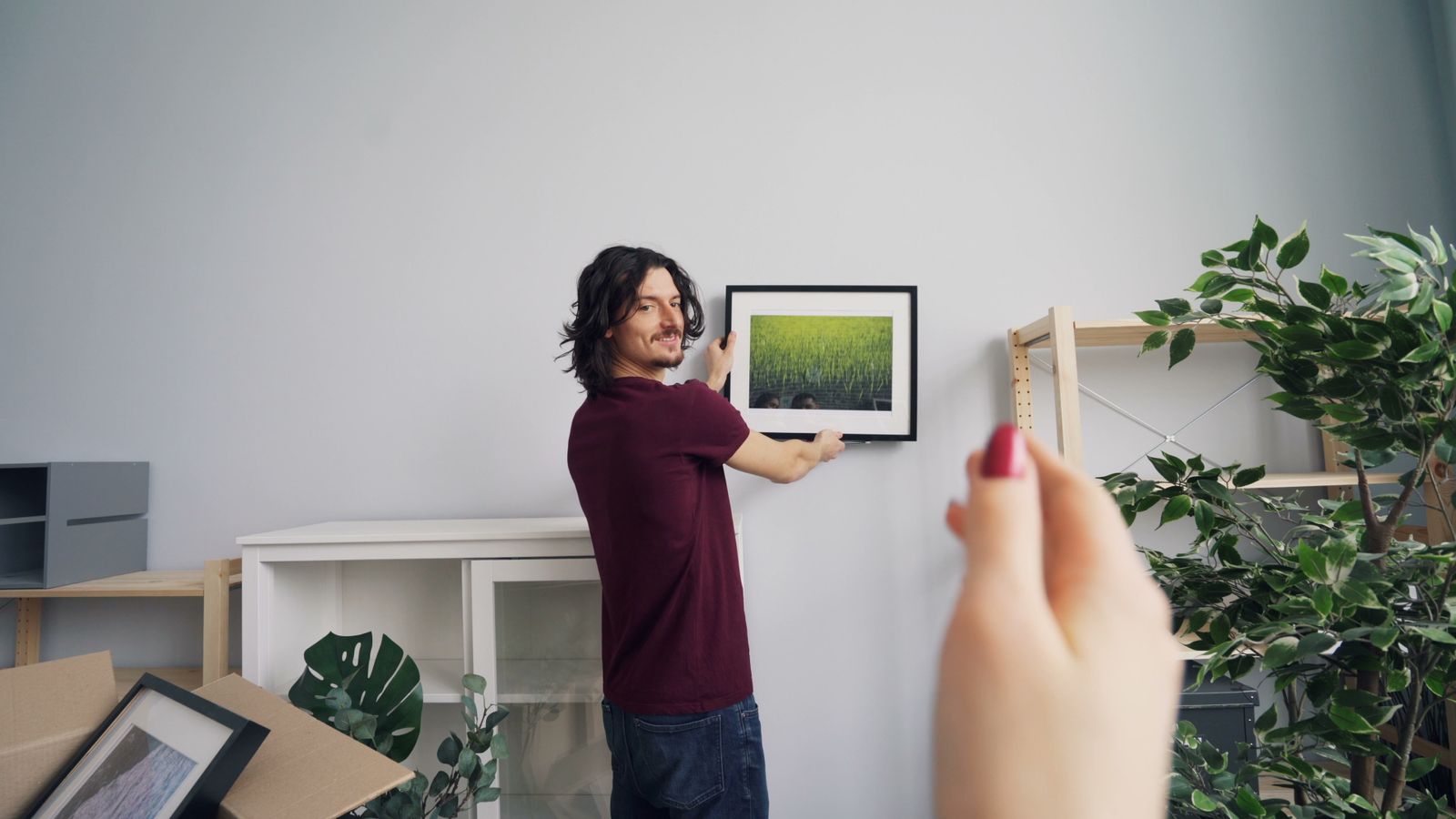 Person hanging a framed picture on a wall using a level and hardware