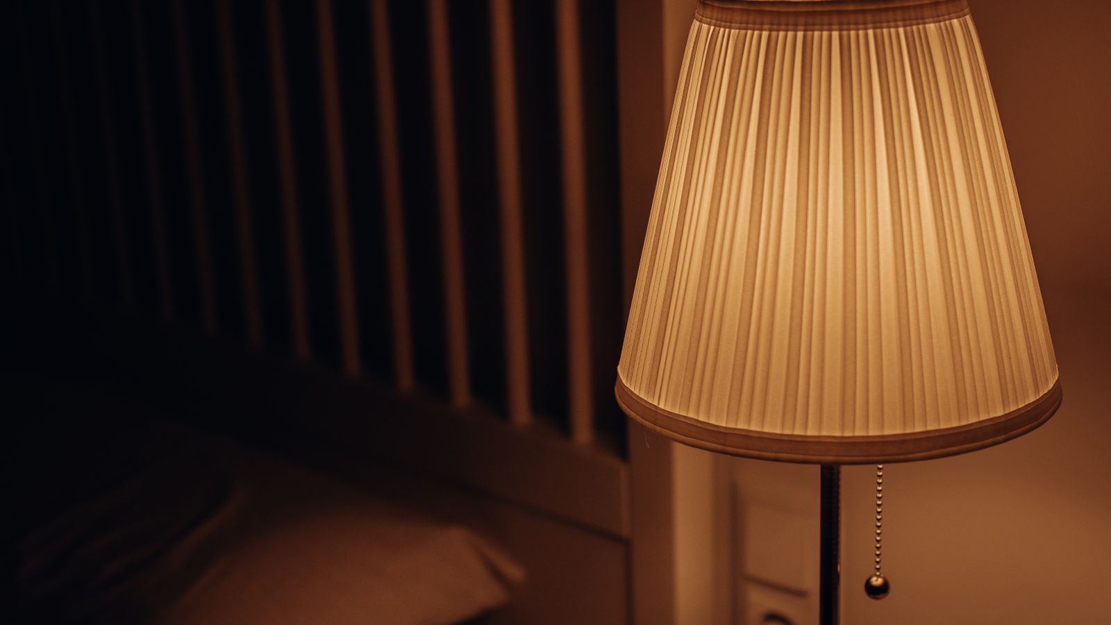 Bedside lamp and small alarm clock arranged on a nightstand next to a bed
