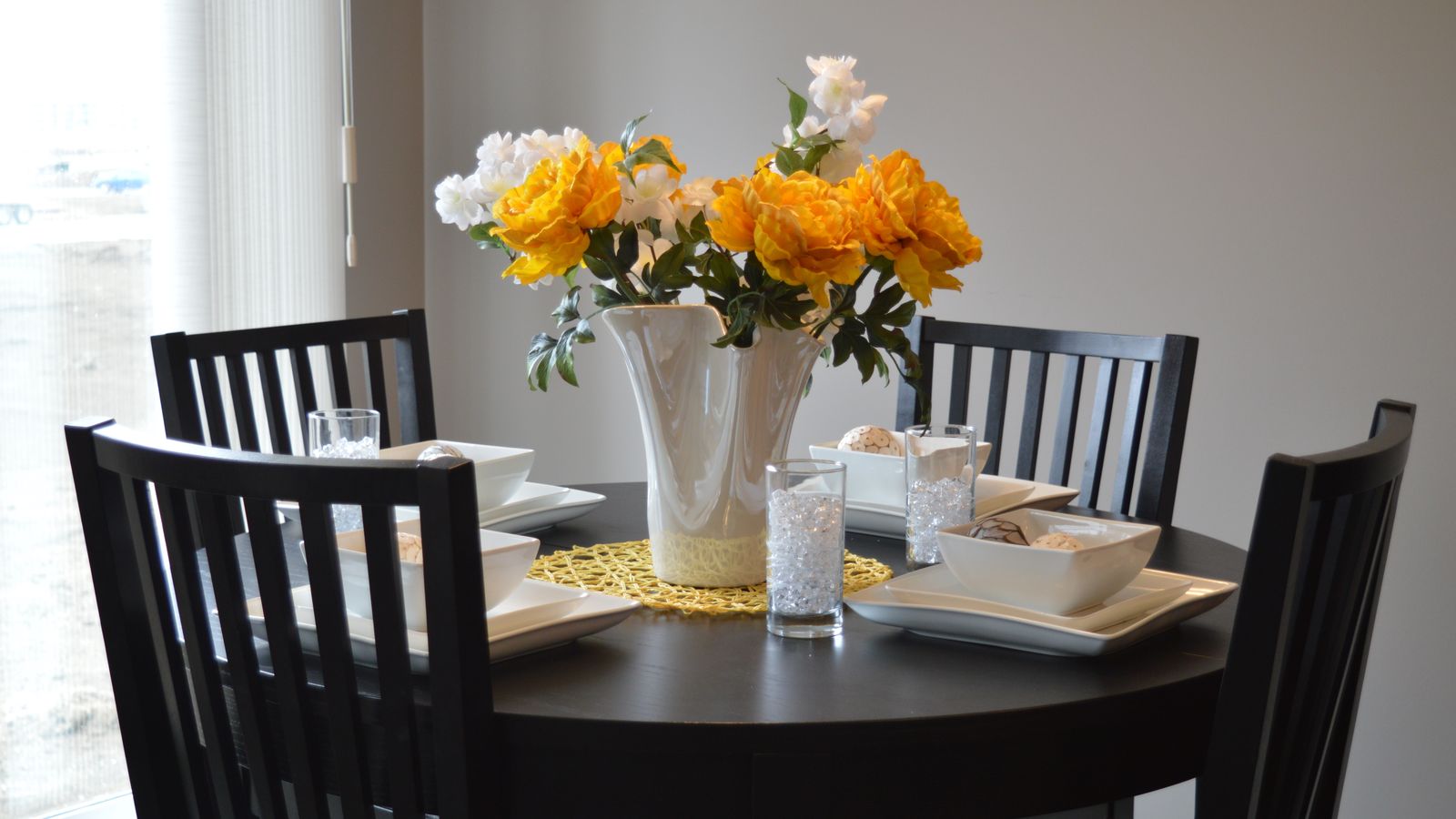 Round wooden dining table set for a meal in a bright dining room