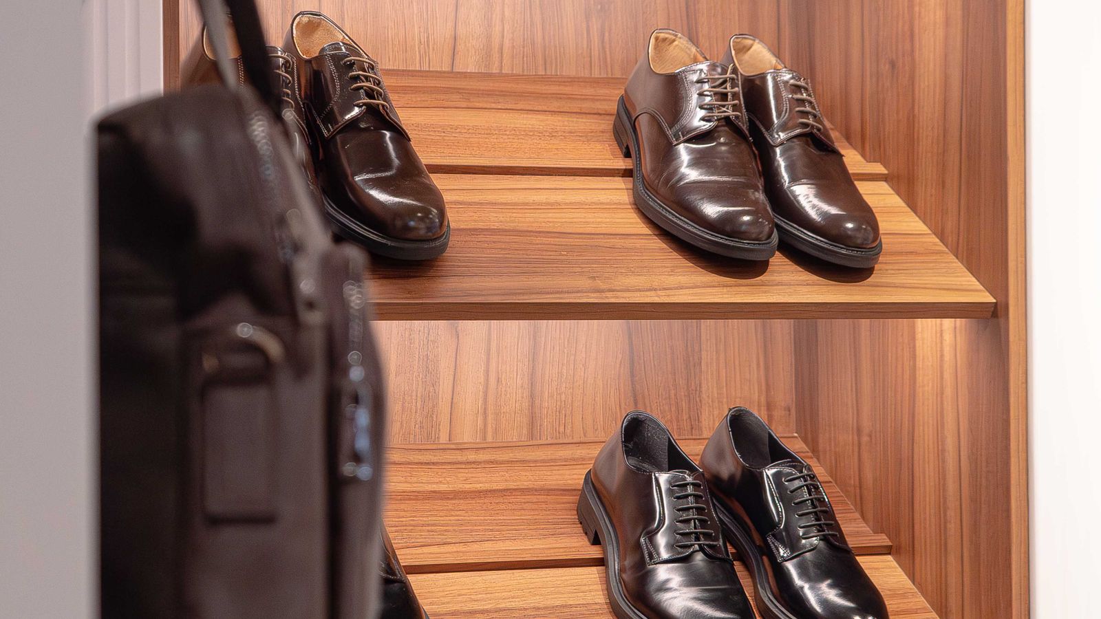 Close-up of dress shoes arranged on wooden shelving inside a closet