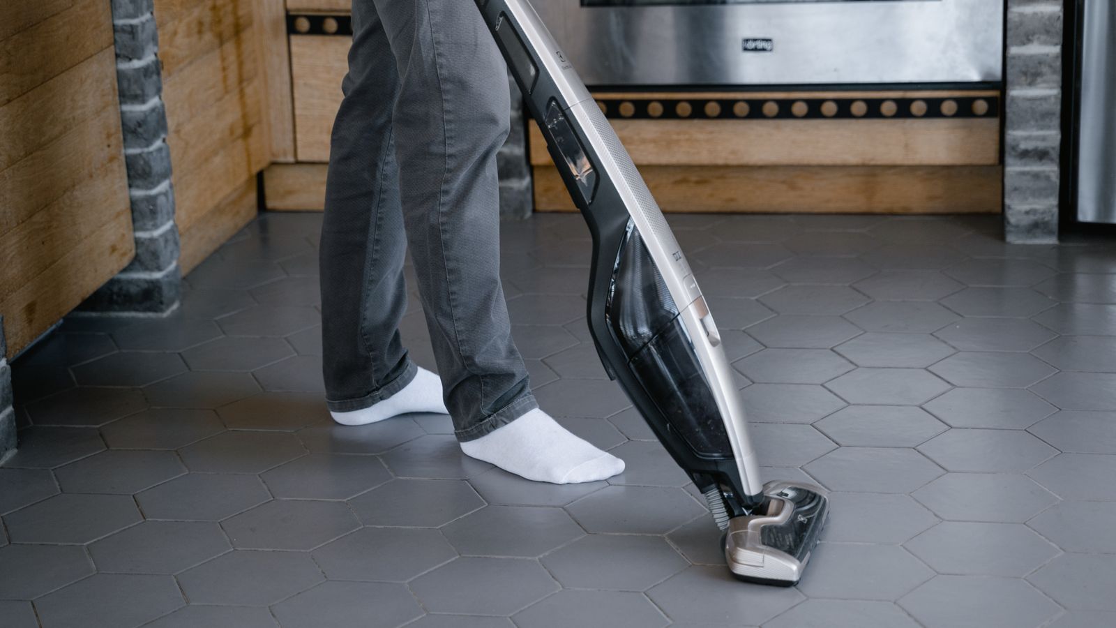Person using a cordless stick vacuum to clean a hardwood living room floor